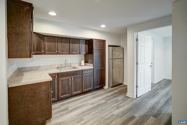 kitchen featuring freestanding refrigerator, a sink, dark brown cabinets, light wood finished floors, and light countertops