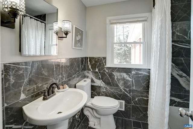 bathroom with a sink, tile walls, toilet, a chandelier, and a wainscoted wall