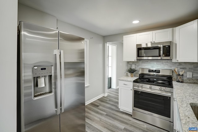 kitchen featuring appliances with stainless steel finishes, white cabinets, light wood finished floors, tasteful backsplash, and baseboards