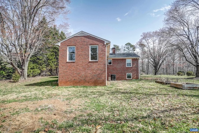 view of property exterior featuring a vegetable garden, brick siding, and a lawn