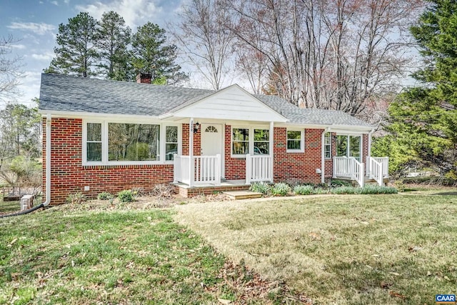 view of front facade with a chimney, a front yard, brick siding, and roof with shingles