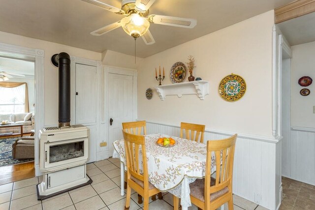 121 Central St S, Broadway, VA 22815 - dining space featuring a ceiling fan, a wood stove, a wainscoted wall, and light tile patterned floors