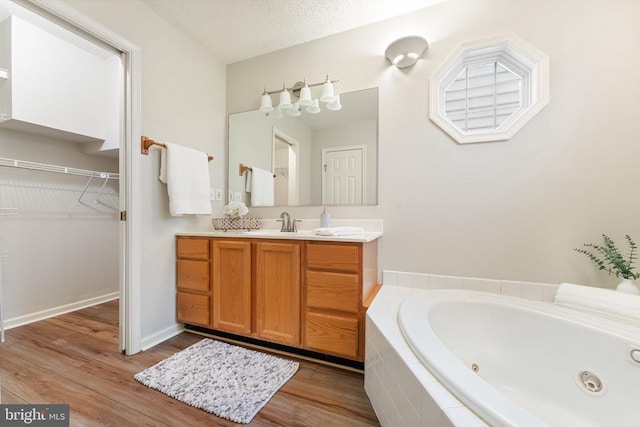 bathroom featuring a spacious closet, a textured ceiling, vanity, wood finished floors, and a jetted tub