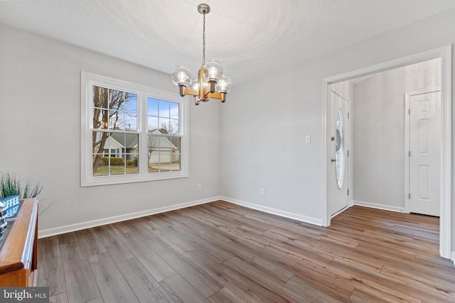 unfurnished dining area featuring an inviting chandelier, a textured ceiling, baseboards, and wood finished floors