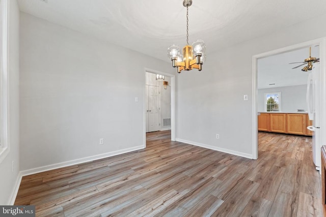 unfurnished dining area with ceiling fan with notable chandelier, light wood-type flooring, visible vents, and baseboards