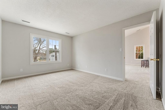 spare room featuring carpet floors, baseboards, visible vents, and a textured ceiling