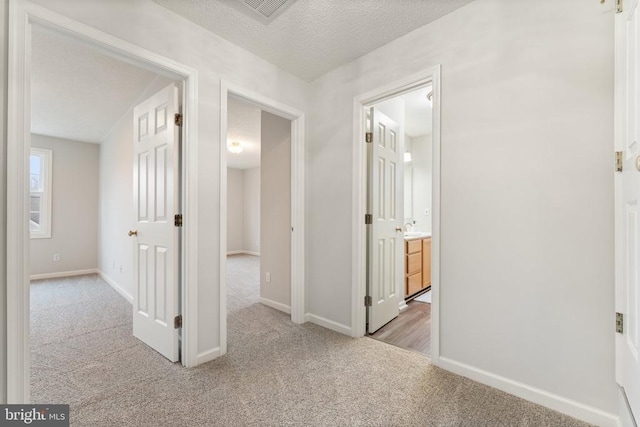 hallway featuring carpet, a sink, a textured ceiling, and baseboards