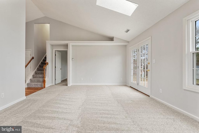 unfurnished living room with carpet floors, lofted ceiling with skylight, stairs, and baseboards