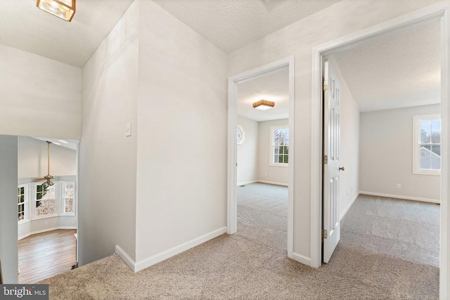 corridor featuring carpet, a textured ceiling, and baseboards