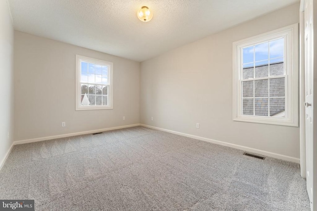 unfurnished room with baseboards, carpet, visible vents, and a textured ceiling