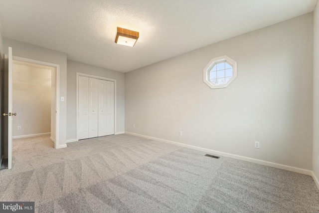 unfurnished bedroom with visible vents, baseboards, carpet, a textured ceiling, and a closet