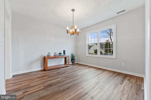 unfurnished dining area featuring visible vents, an inviting chandelier, light wood-style floors, a textured ceiling, and baseboards