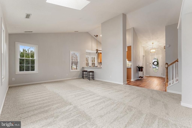 unfurnished living room with carpet, visible vents, vaulted ceiling with skylight, baseboards, and stairs