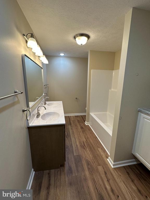 218 Honeyville Rd, Stanley, VA 22851 - full bathroom featuring wood finished floors, double vanity, baseboards, a textured ceiling, and shower / tub combination
