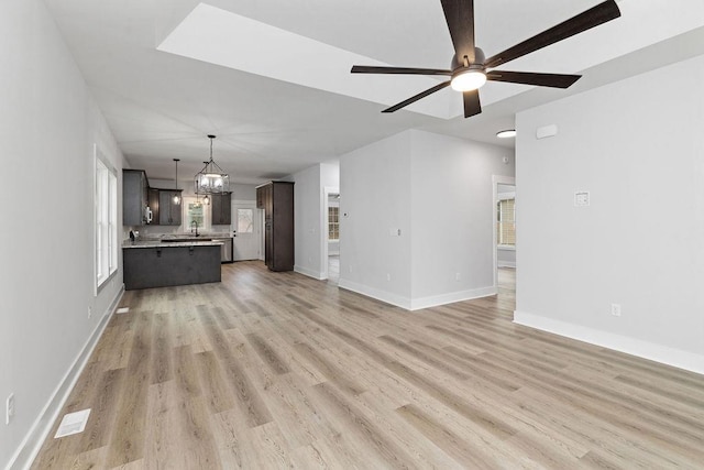 unfurnished living room with ceiling fan with notable chandelier, sink, and light hardwood / wood-style floors