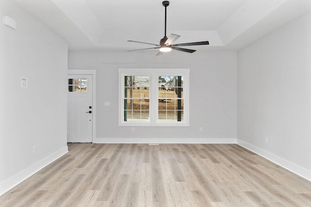 unfurnished room featuring ceiling fan, a tray ceiling, and light wood-type flooring