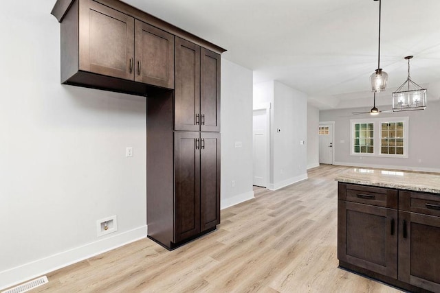 kitchen with light stone counters, light hardwood / wood-style flooring, dark brown cabinets, a notable chandelier, and pendant lighting