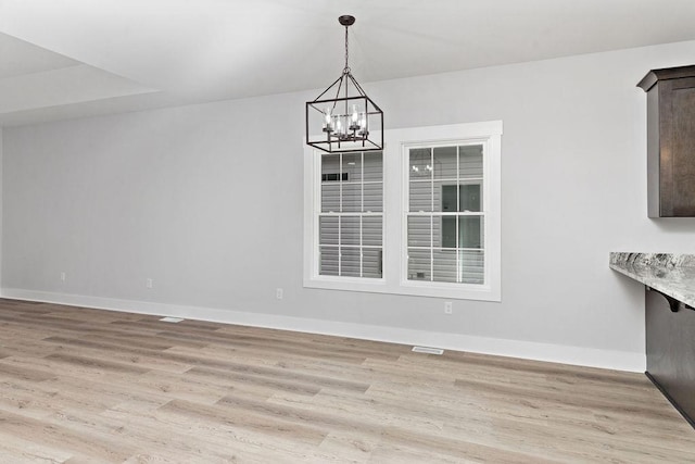 unfurnished dining area featuring an inviting chandelier and light wood-type flooring