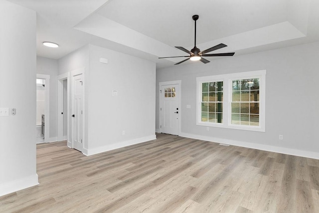 unfurnished room featuring ceiling fan, light wood-type flooring, and a tray ceiling