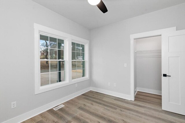 unfurnished bedroom featuring wood-type flooring, a spacious closet, ceiling fan, and a closet