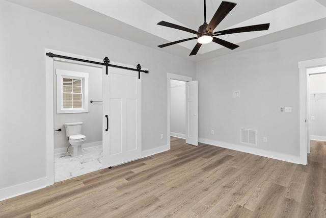 unfurnished bedroom featuring a barn door, a spacious closet, and light hardwood / wood-style floors