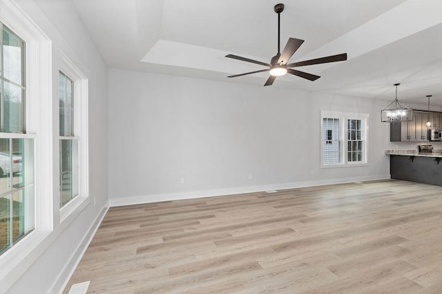 unfurnished living room with ceiling fan with notable chandelier and light wood-type flooring