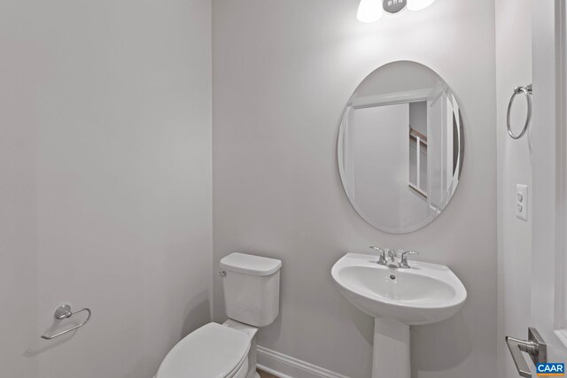 half bath featuring toilet, baseboards, and a sink