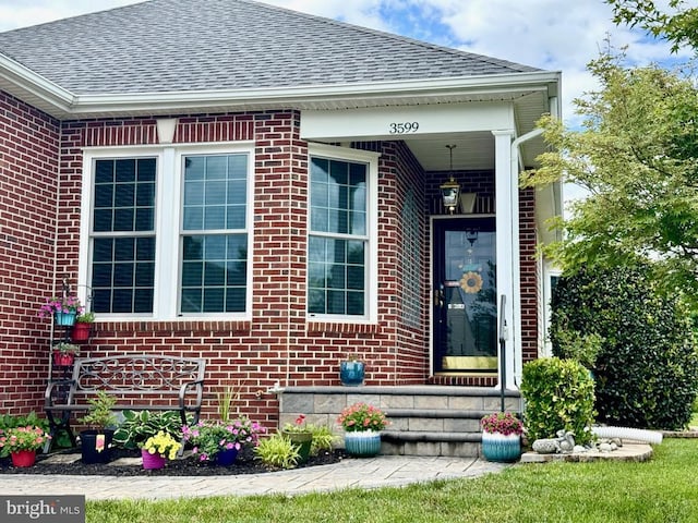  - view of exterior entry with a shingled roof and brick siding