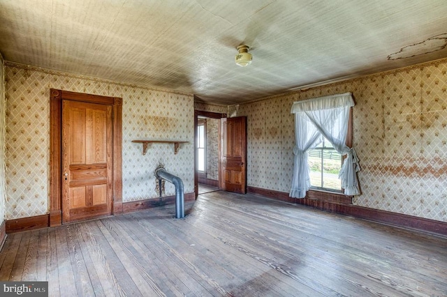 unfurnished living room featuring hardwood / wood-style flooring, plenty of natural light, wallpapered walls, baseboards, and crown molding