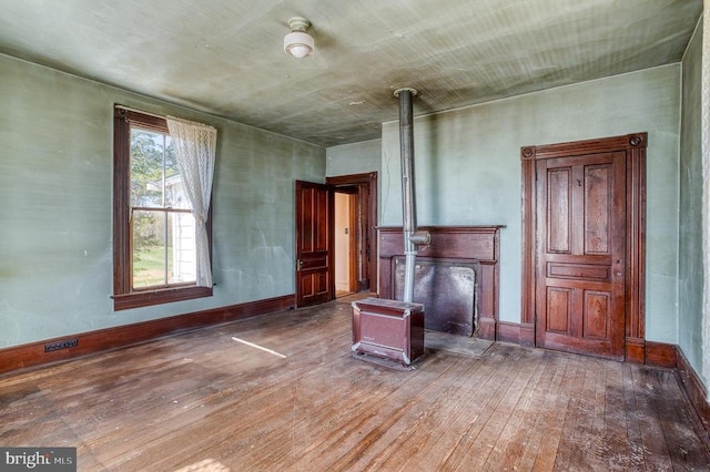 unfurnished living room with wood-type flooring, a wood stove, and baseboards