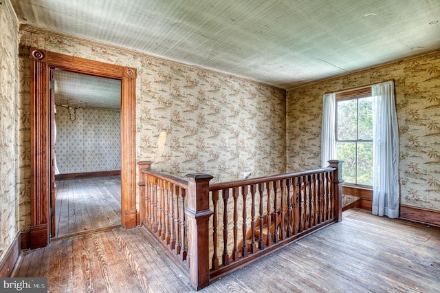 hall featuring an upstairs landing, hardwood / wood-style flooring, baseboards, and wallpapered walls