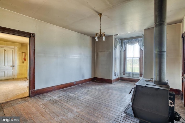 unfurnished dining area with a wood stove, wood-type flooring, and baseboards