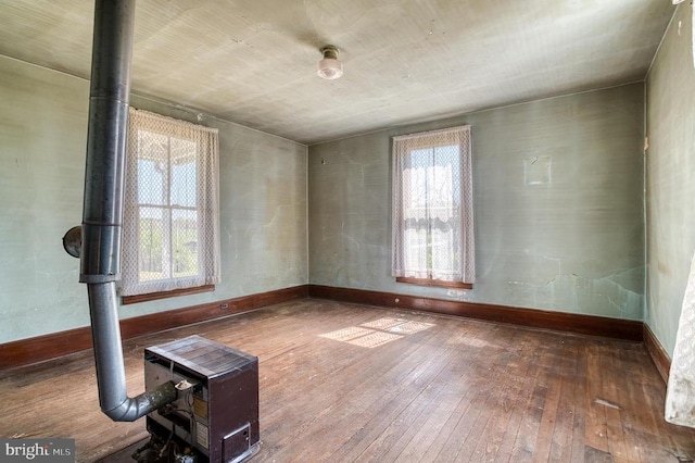 spare room featuring a wood stove, hardwood / wood-style floors, and baseboards