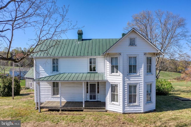 rear view of house featuring a standing seam roof, a porch, metal roof, a chimney, and a yard