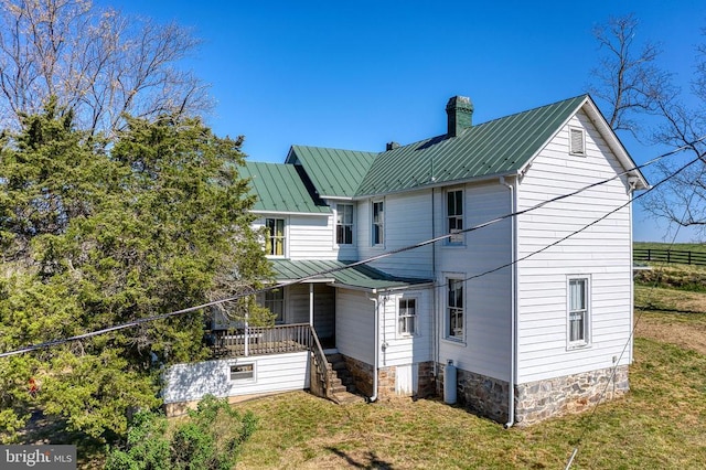 back of property featuring a chimney, a lawn, metal roof, and a standing seam roof