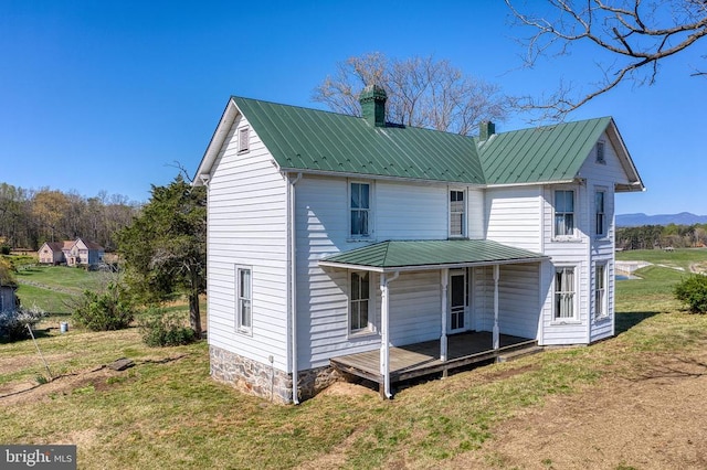 rear view of house featuring a chimney, a lawn, metal roof, and a porch