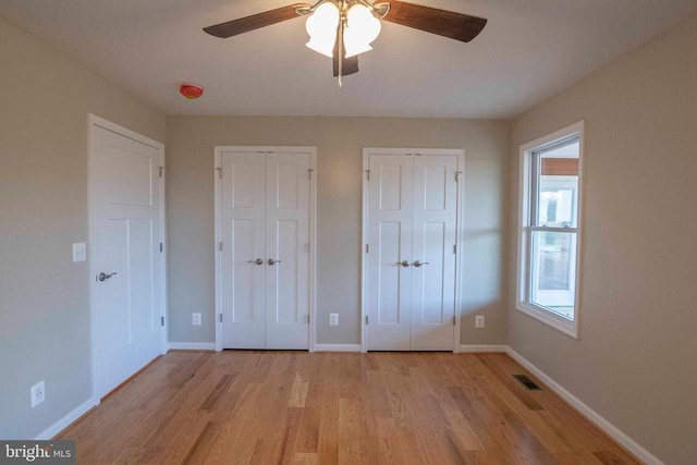 unfurnished bedroom featuring two closets, ceiling fan, and light wood-type flooring