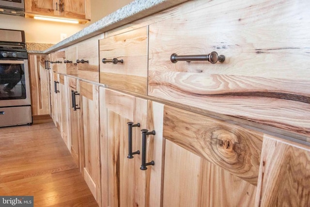 details featuring light stone counters, stainless steel gas range, light hardwood / wood-style floors, and light brown cabinets