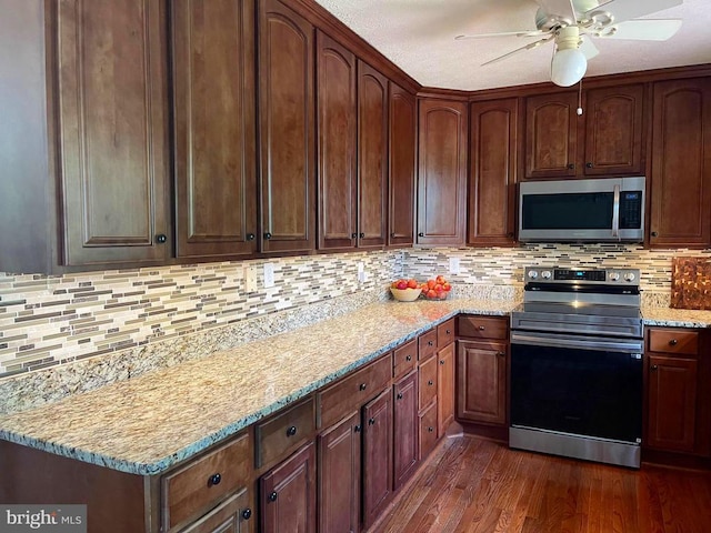 - kitchen with appliances with stainless steel finishes, dark wood finished floors, a ceiling fan, backsplash, and light stone countertops