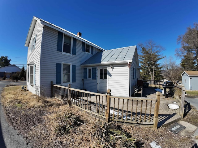 back of house with a chimney, a deck, metal roof, and a standing seam roof