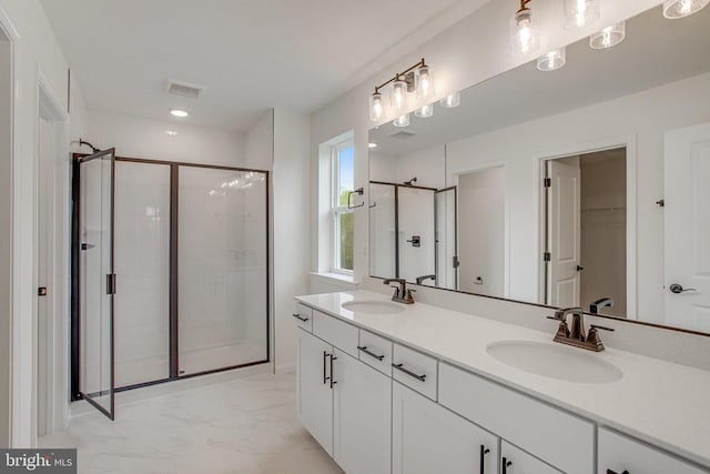full bathroom featuring a shower stall, marble finish floors, double vanity, and a walk in closet