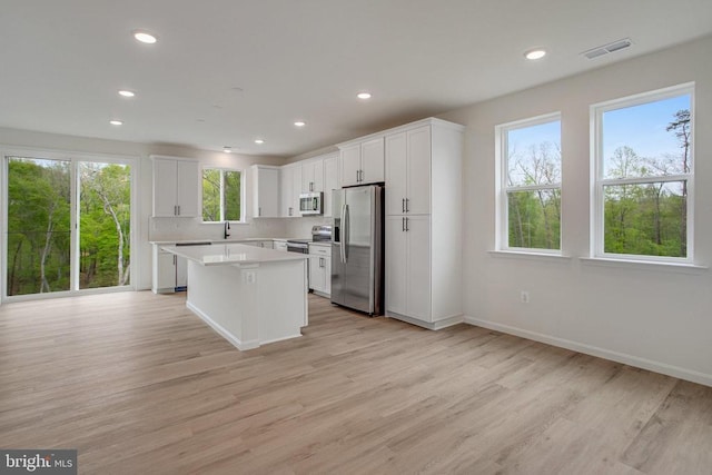 kitchen with stainless steel appliances, a kitchen island, light countertops, light wood finished floors, and recessed lighting