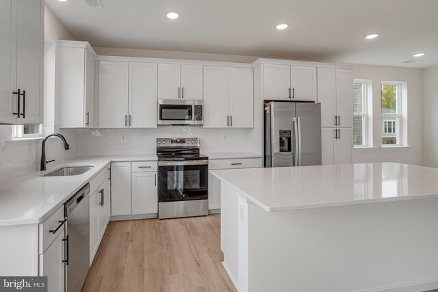 kitchen with stainless steel appliances, a sink, light wood finished floors, white cabinetry, and decorative backsplash