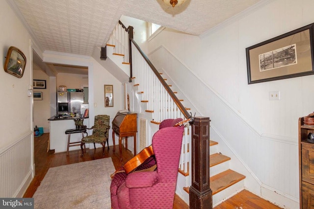 staircase featuring an ornate ceiling, wood finished floors, ornamental molding, and a decorative wall