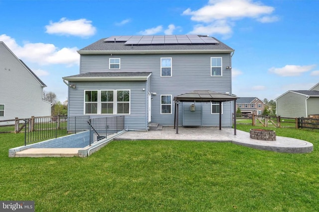 rear view of house featuring a gazebo, a patio, solar panels, a lawn, and an outdoor fire pit