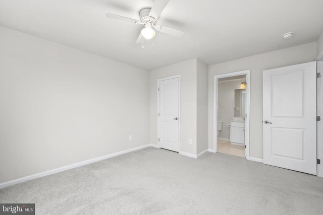 unfurnished bedroom featuring baseboards, ensuite bath, a ceiling fan, and light colored carpet