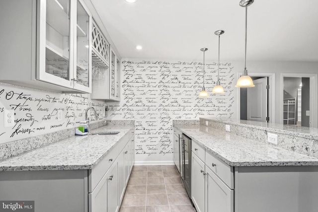 kitchen featuring light stone countertops, beverage cooler, glass insert cabinets, a sink, and a peninsula