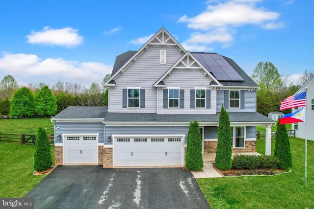 craftsman-style home with an attached garage, fence, a front lawn, solar panels, and driveway
