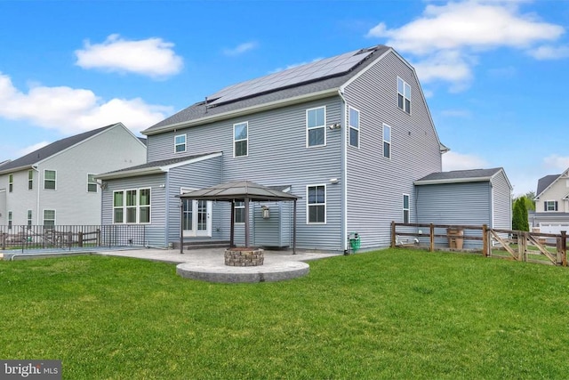 back of property featuring a yard, a patio area, a fire pit, a fenced backyard, and roof mounted solar panels