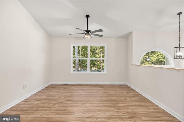 empty room featuring ceiling fan with notable chandelier and light hardwood / wood-style floors